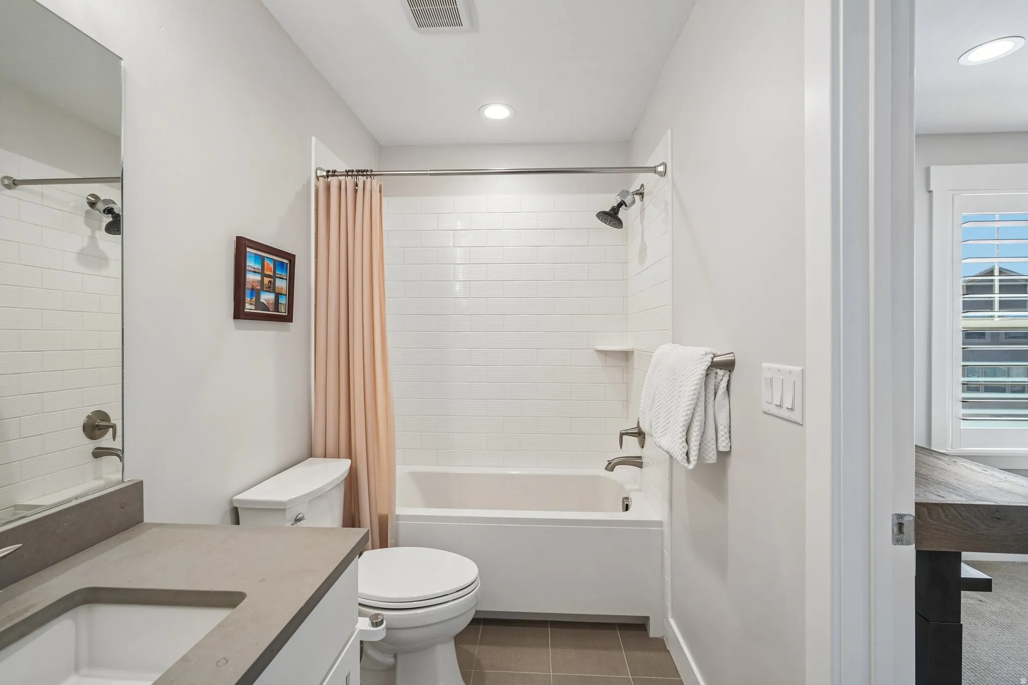 Full bathroom featuring a single vanity with an integrated sink and light-toned countertop, a shower-over-tub with white subway tile surround, and recessed lighting