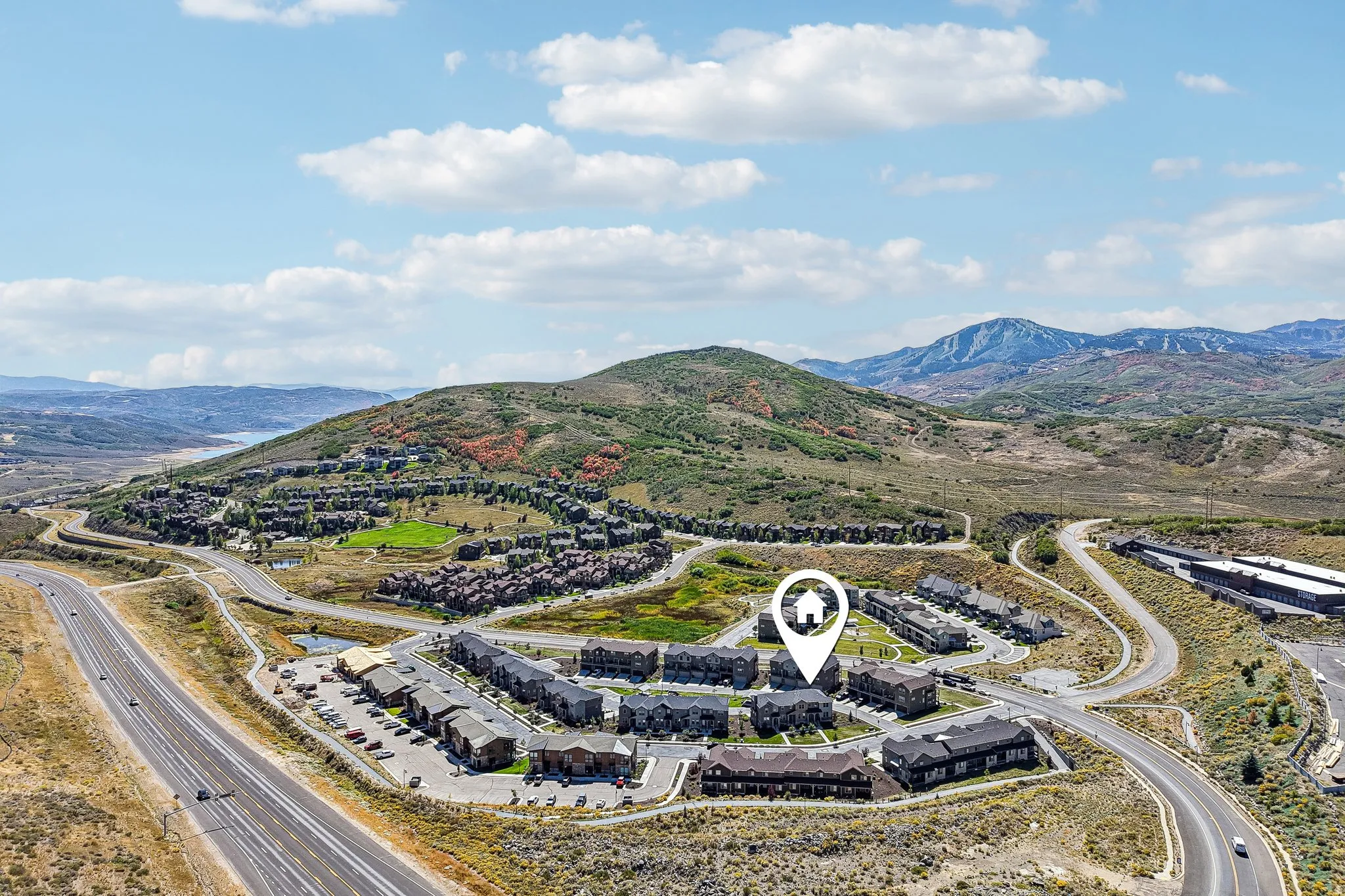 Aerial perspective with surrounding mountainous terrain, multiple residential structures, and a prominent roadway