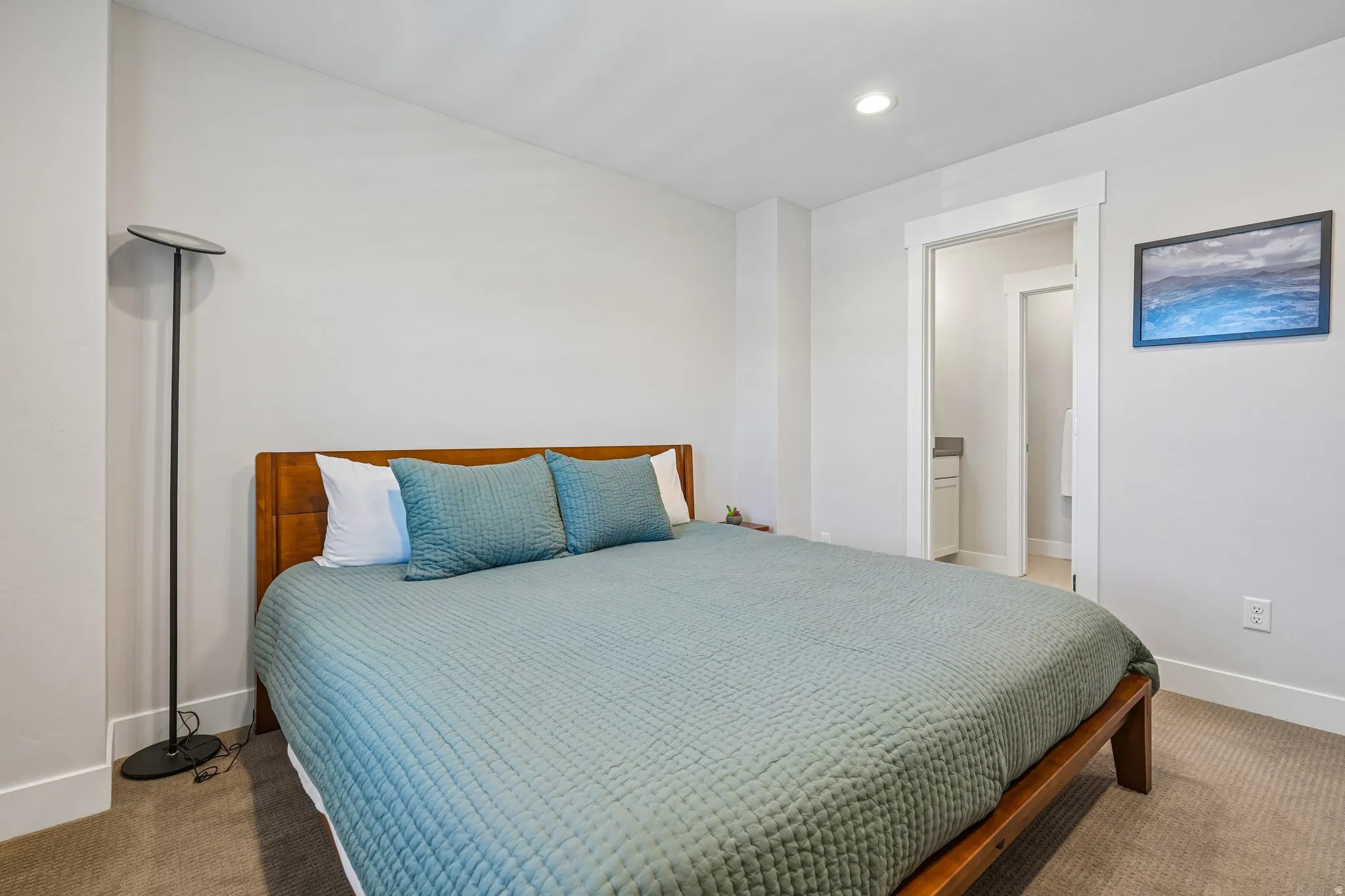 Recessed ceiling lighting, wood-finish headboard, white trim, carpeted flooring, and an adjoining bathroom
