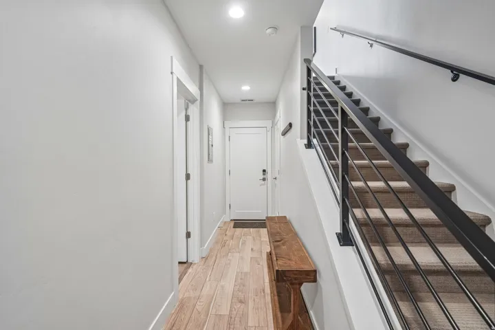 Wood-finish flooring, recessed lighting, white doors, and a staircase with metal railings and carpeted treads