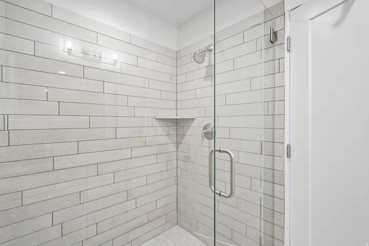 Glass-enclosed shower with horizontal wall tiling, built-in shelf, rainfall showerhead, and brushed nickel fixtures