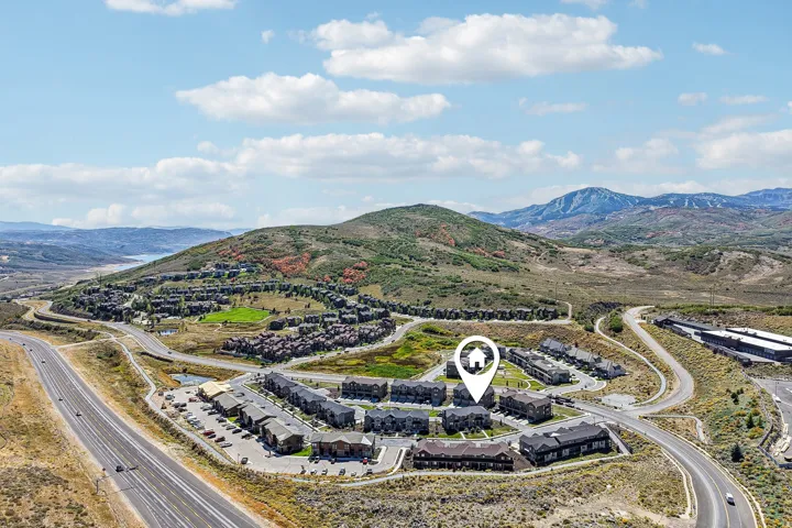 Aerial perspective with surrounding mountainous terrain, multiple residential structures, and a prominent roadway