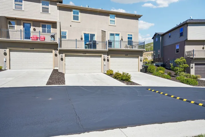 Multi-level townhome featuring a neutral stucco exterior, private balconies with metal railings, and attached garages