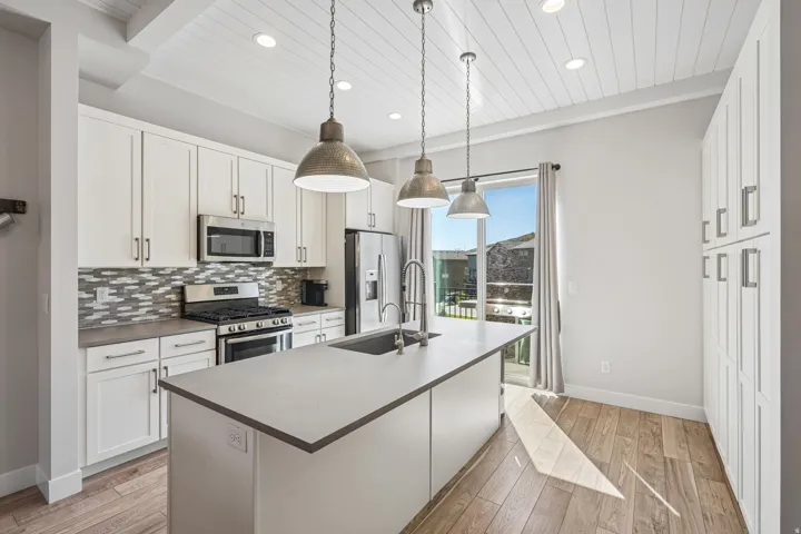 Kitchen featuring white cabinetry, stainless steel appliances, a center island with an undermount sink, and wood-finish flooring