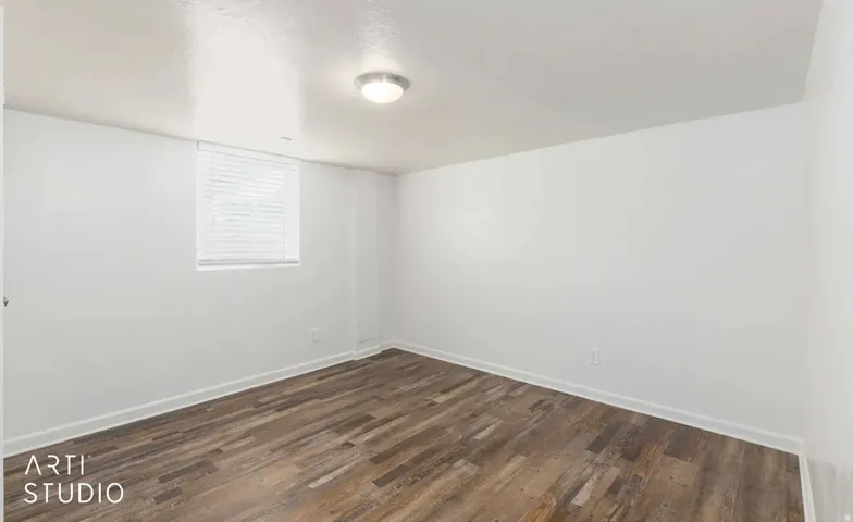 Wood-finish flooring, white walls, flush mount ceiling light, and window with blinds