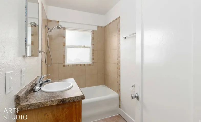 Bathroom featuring a single vanity with an integrated sink, a built-in bathtub, a shower with a handheld fixture, and tile surround with decorative accents
