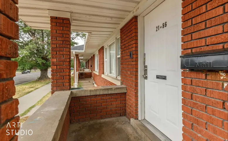 Brick exterior with white paneled door, black wall-mounted mailbox, and concrete porch