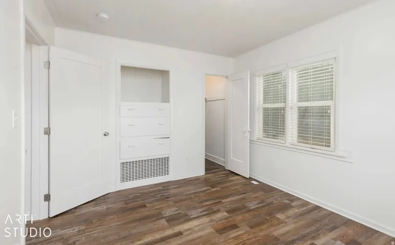 Wood-finish flooring, white walls, built-in drawer storage, and a double window with blinds