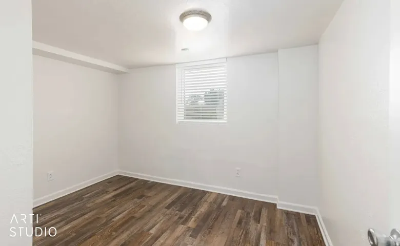 Wood-finish flooring with white trim, a single window with blinds, and recessed ceiling lighting