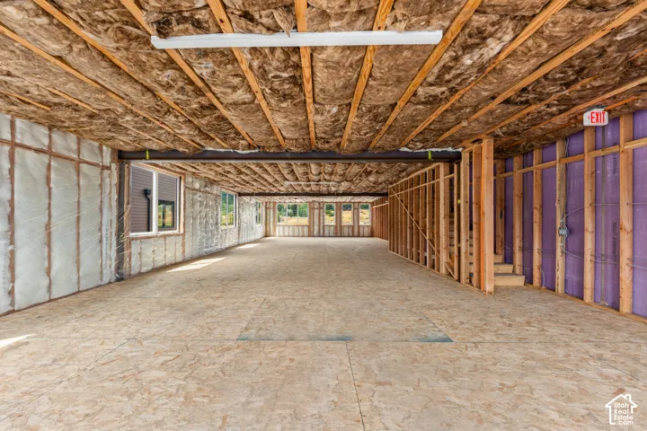 Expansive unfinished space featuring exposed ceiling joists, wood-finish subflooring, multiple windows, and a partially framed wall with purple insulation