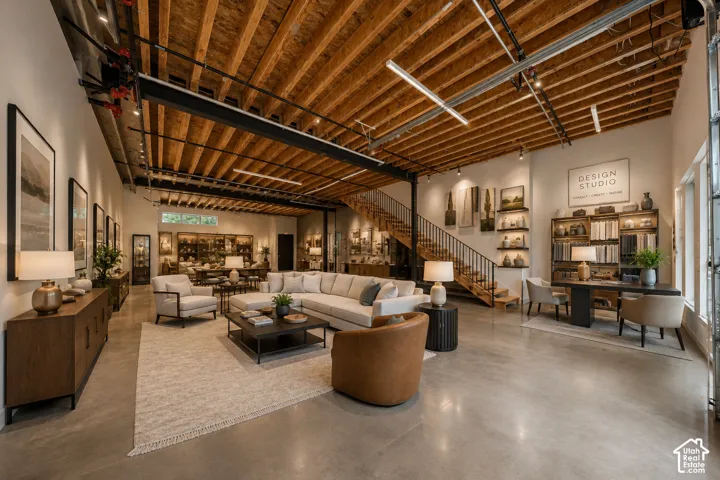 Exposed wood beam ceiling, concrete flooring, open-tread staircase with metal railing, built-in wall shelving, and large windows
