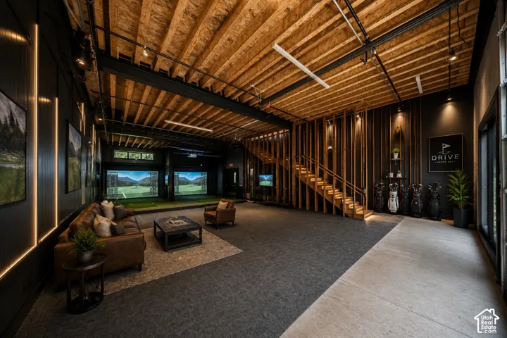 Exposed wood beam ceiling, contemporary track lighting, built-in golf simulator bays, wood-finish slatted wall detailing, and a concrete flooring section
