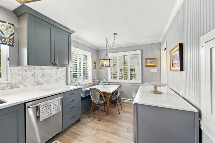 Gray shaker-style cabinetry with matte black hardware, stainless steel dishwasher, white subway tile backsplash, white countertops, and wood-finish flooring
