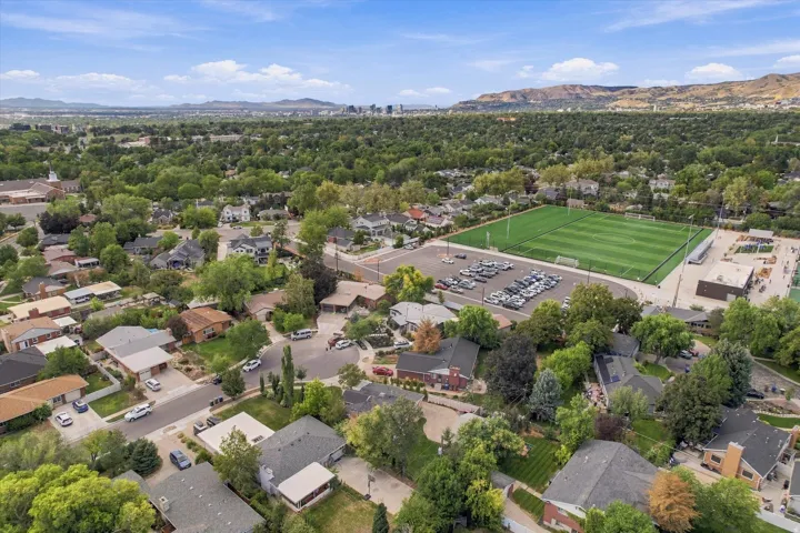 Aerial perspective of a verdant neighborhood with established trees, nearby sports complex, and distant city skyline