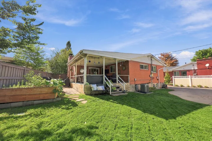 Brick exterior featuring a covered patio, raised garden bed, stone pathway, and a detached structure