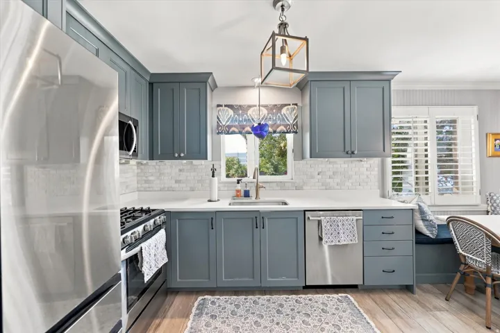 Kitchen featuring blue shaker-style cabinetry, white countertops, tile backsplash, stainless steel appliances, and wood-finish flooring