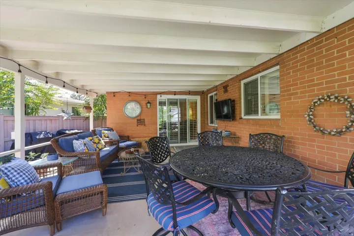 Covered patio featuring an exposed beam ceiling, brick exterior wall, sliding glass door, and a privacy fence