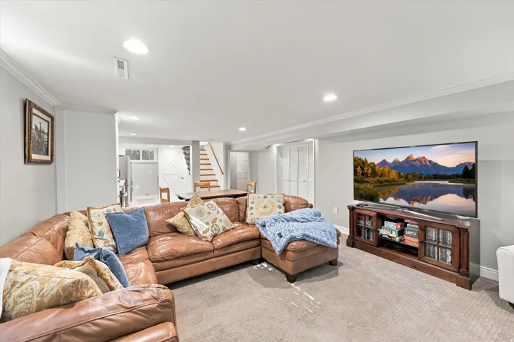 Recessed lighting, crown molding, light-toned carpeting, wood staircase, and a built-in entertainment console