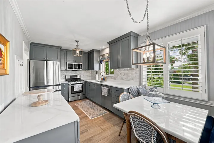 Kitchen featuring shaker-style cabinetry, stainless steel appliances, wood-finish flooring, white countertops, and a subway tile backsplash