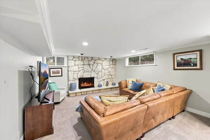Spacious room with a stone-clad fireplace and hearth, recessed lighting, crown molding, and carpeting