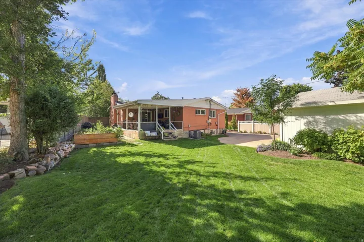 Expansive lawn area, covered patio, raised garden bed, mature trees, and a paved driveway