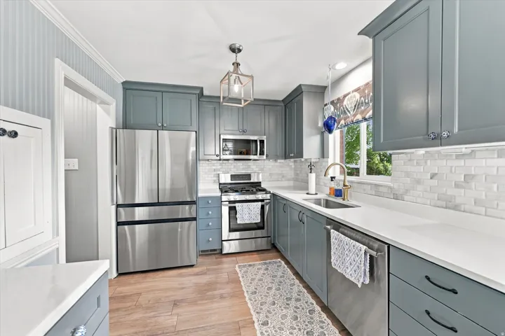 Contemporary kitchen featuring shaker-style cabinetry, stainless steel appliances, white countertops, and a subway tile backsplash