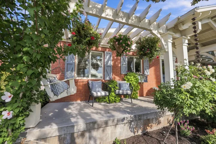 Brick exterior with a white pergola, concrete porch, and established landscaping