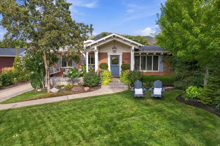 Brick exterior with white trim, covered front porch, front yard with mature landscaping, and an asphalt driveway
