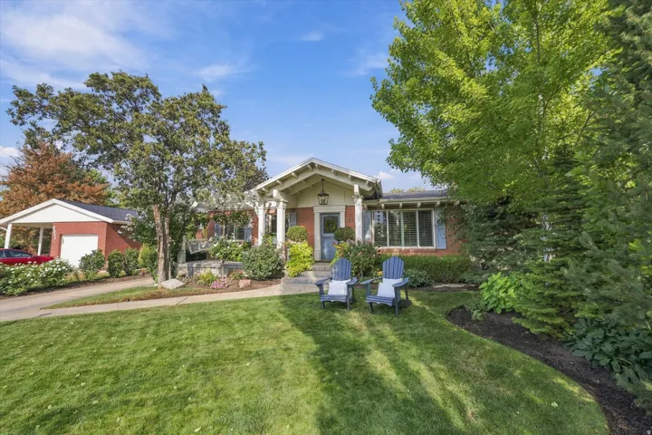 Brick exterior with painted shutters, columned front porch, established landscaping, and a detached two-car garage with an attached carport