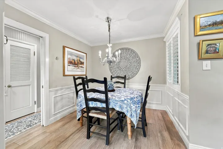 Dining area featuring light wood-finish flooring, wainscoting, crown molding, and a chandelier