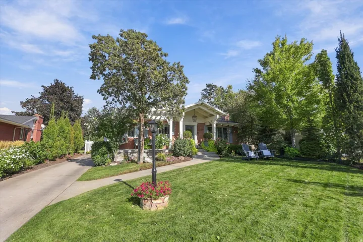 Manicured front lawn with mature trees, a paved driveway, and established landscaping leading to a covered entry