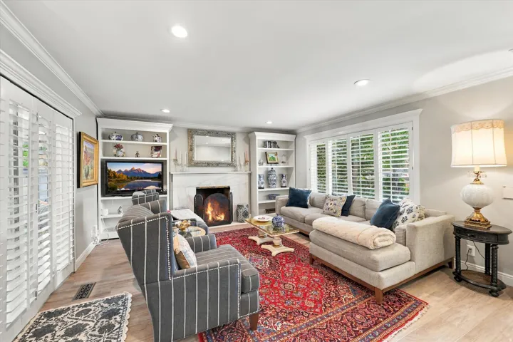 Living area featuring built-in shelving, wood-finish flooring, a fireplace with a stone surround, recessed lighting, and plantation shutters