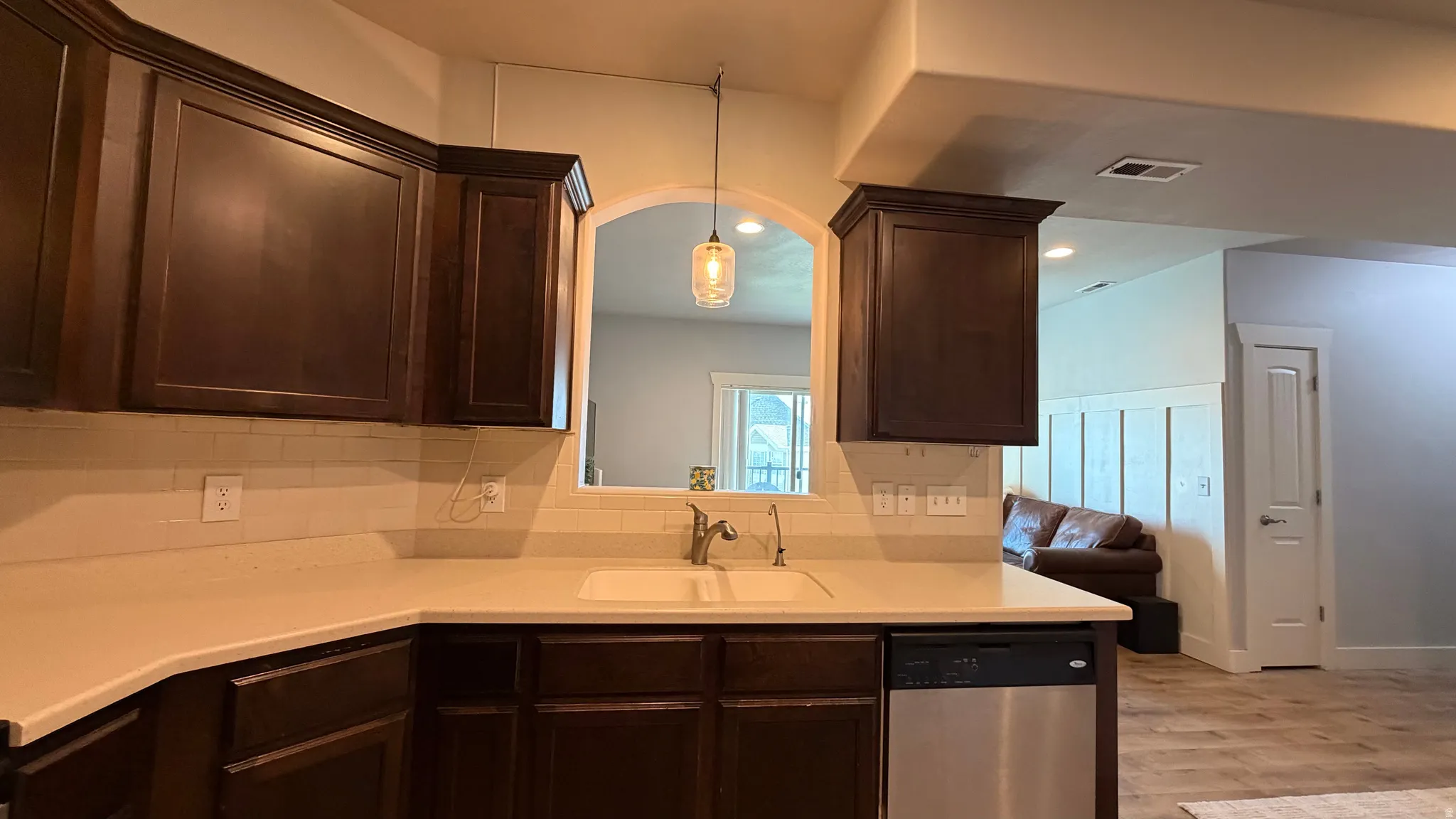 Dark wood-finish cabinetry, light countertops, subway tile backsplash, stainless steel dishwasher, and an arched pass-through opening
