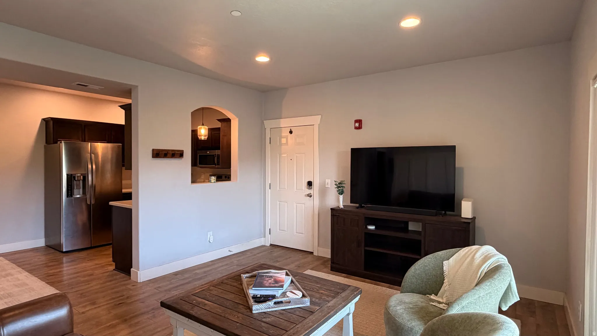 Recessed ceiling lighting, wood-finish flooring, white trim, arched pass-through window, and stainless steel refrigerator