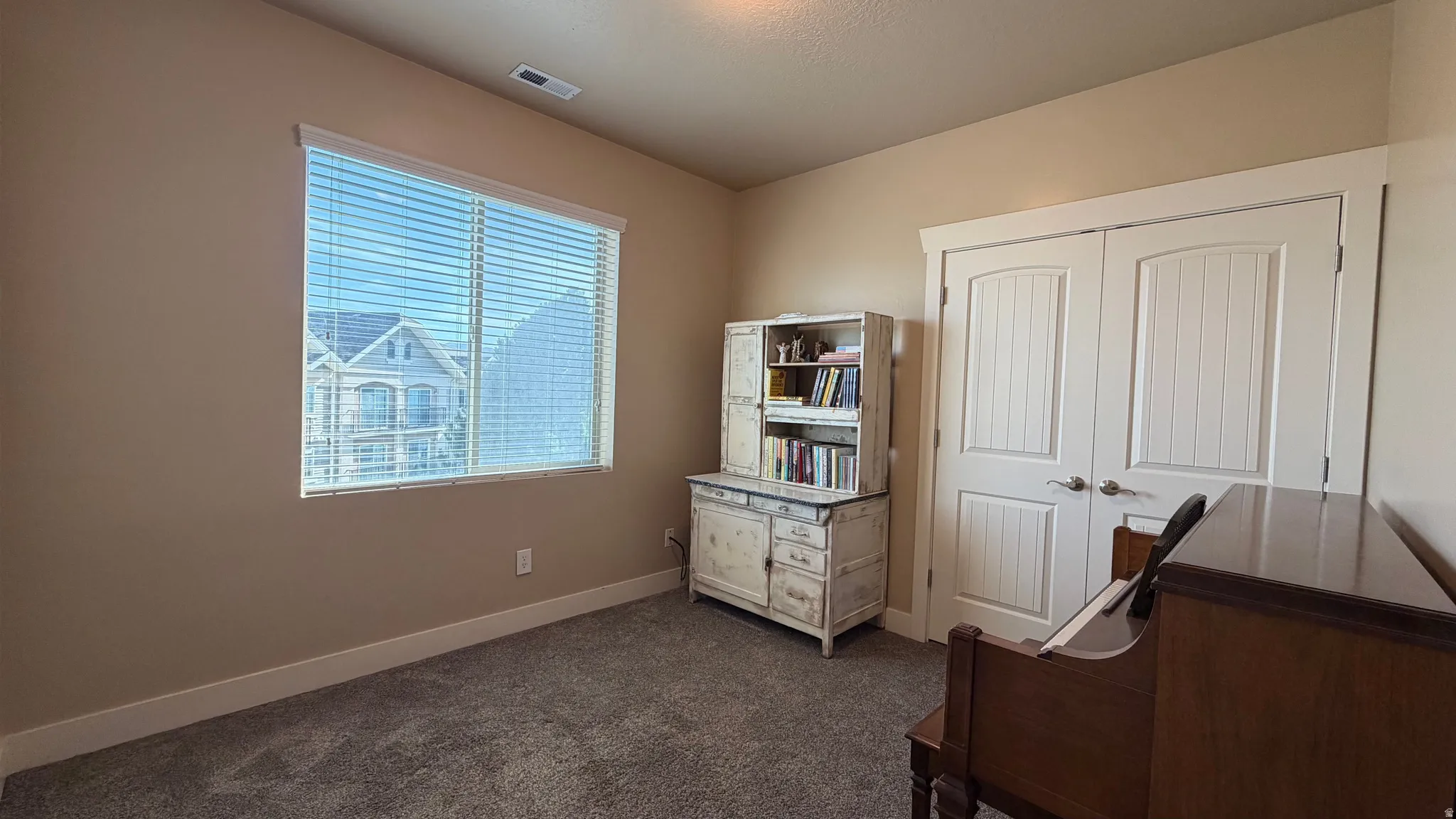 Wall-to-wall carpeting, window with horizontal blinds, and a double-door closet with paneled doors