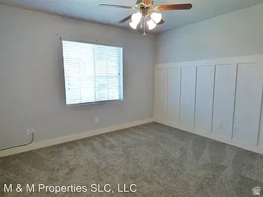 Paddle-style ceiling fan with integrated lighting, window with horizontal blinds, board and batten accent wall, and wall-to-wall carpeting