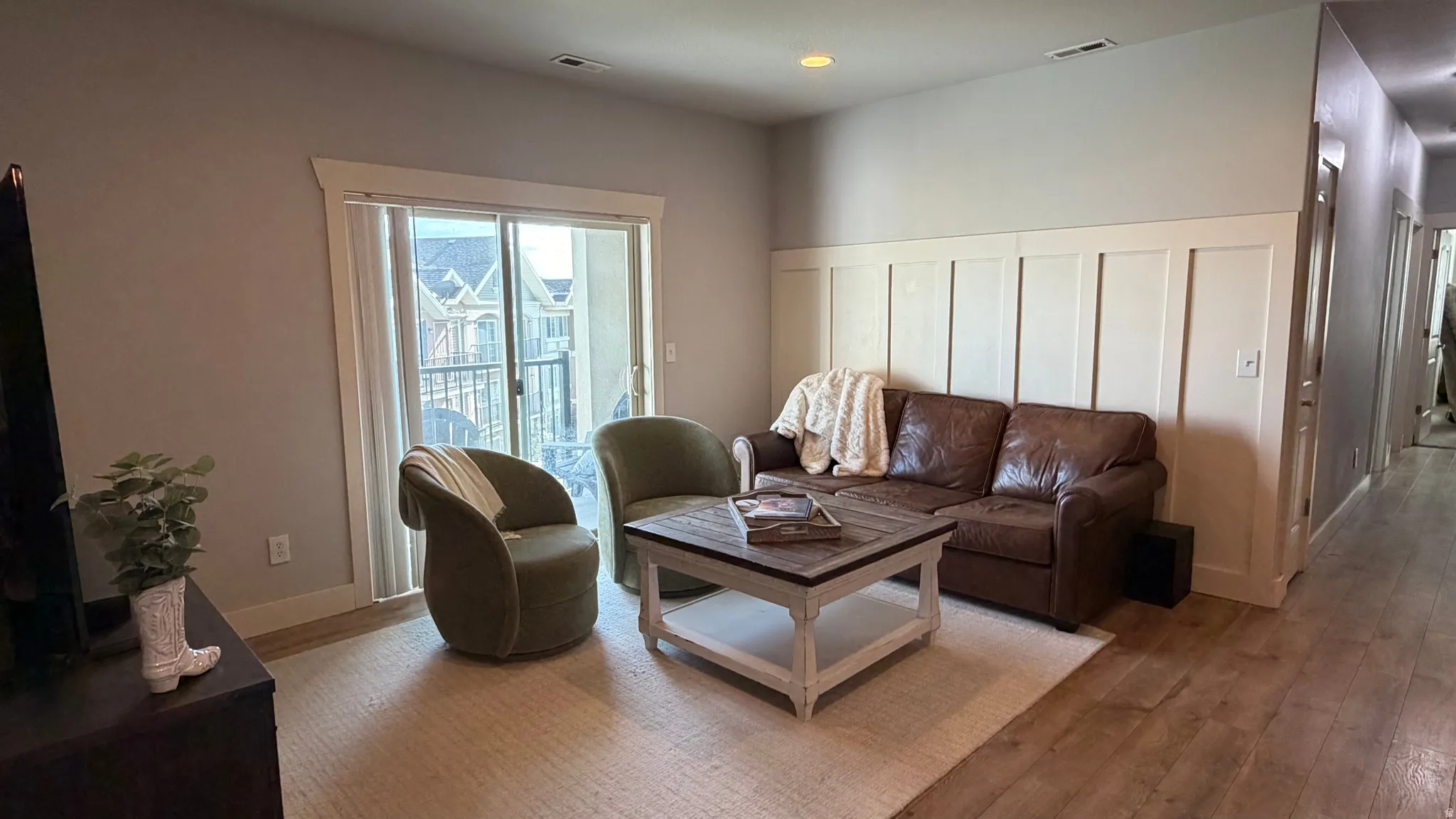 Wood-finish flooring throughout, board and batten wall detailing, sliding glass door with balcony access, recessed lighting, and white trim