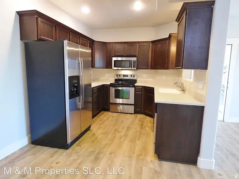 Kitchen featuring wood-finish flooring, stainless steel appliances, dark wood cabinetry, white countertops, and a tile backsplash