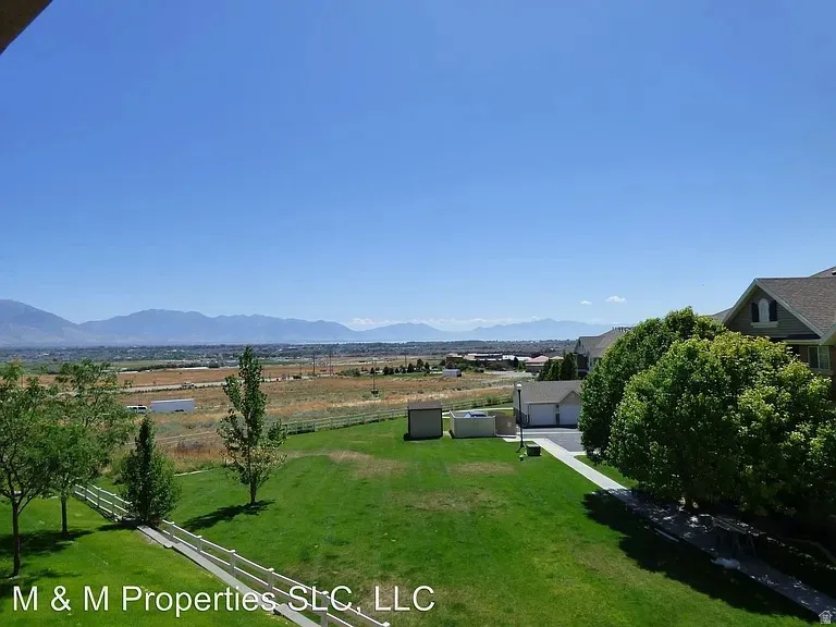 Expansive green lawn with mature trees and a white picket fence, backed by a distant mountain range under a clear sky