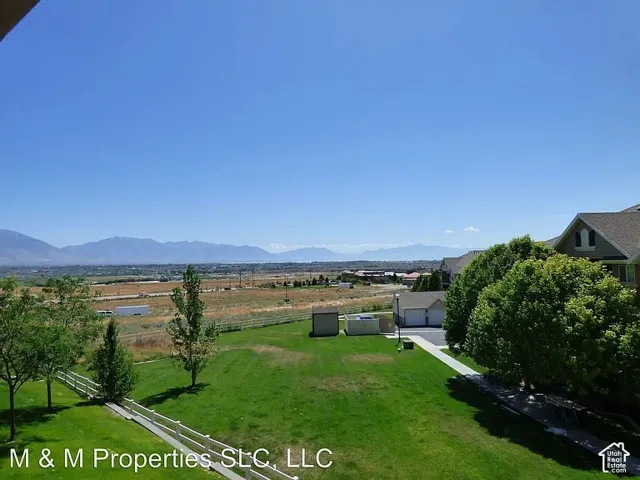 Expansive green lawn with mature trees and a white picket fence, backed by a distant mountain range under a clear sky