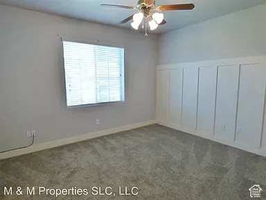 Paddle-style ceiling fan with integrated lighting, window with horizontal blinds, board and batten accent wall, and wall-to-wall carpeting