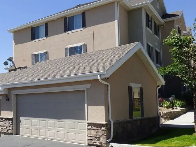 Attached garage with a panel door, stone veneer accents, and stucco exterior