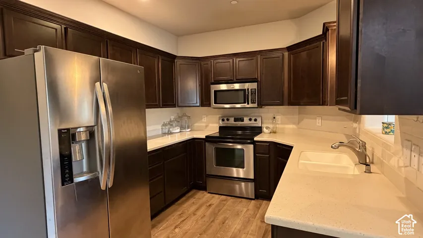 Stainless steel appliances, dark wood-finish cabinetry, light-toned countertops, tile backsplash, and wood-finish flooring