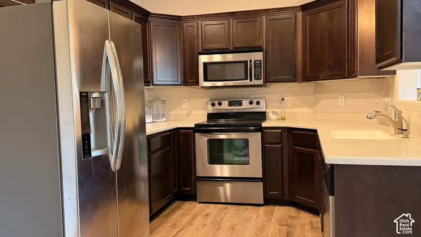 Stainless steel appliances, dark wood cabinetry, light-toned countertops, and wood-finish flooring