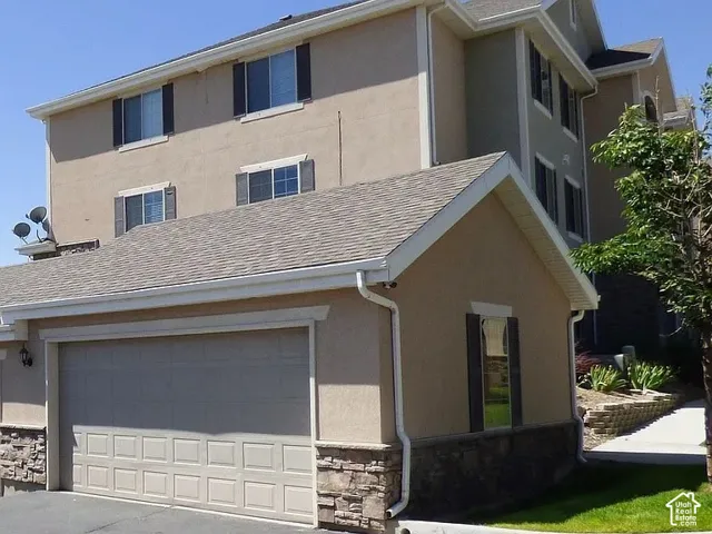 Attached garage with a panel door, stone veneer accents, and stucco exterior