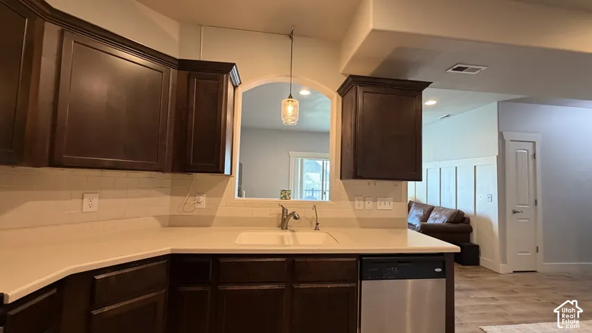 Dark wood-finish cabinetry, light countertops, subway tile backsplash, stainless steel dishwasher, and an arched pass-through opening