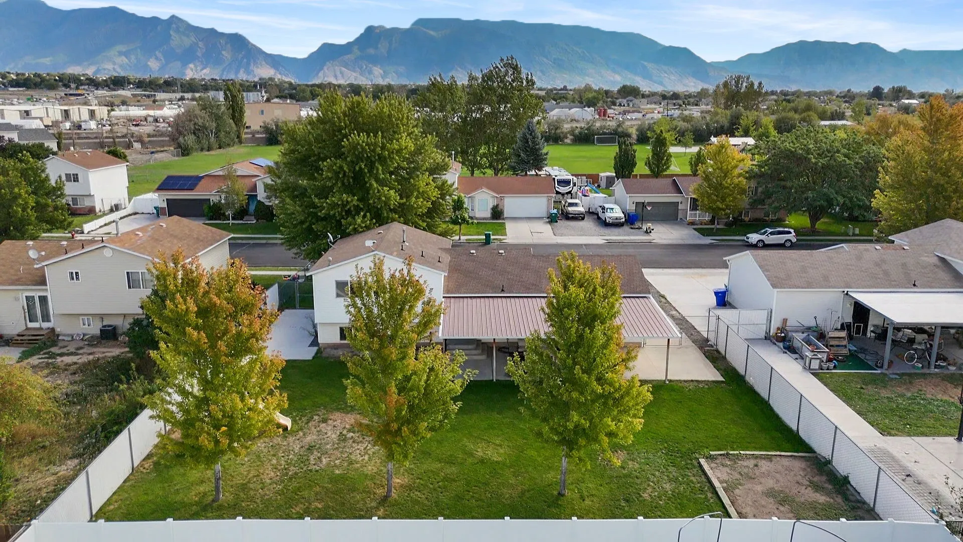 Expansive backyard featuring a manicured lawn, mature trees, and white privacy fencing