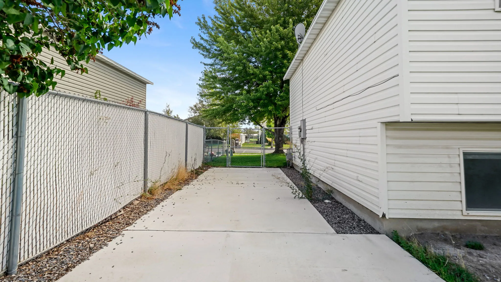 Chain-link fencing with privacy slats, concrete surface, gravel hardscaping, and exterior siding