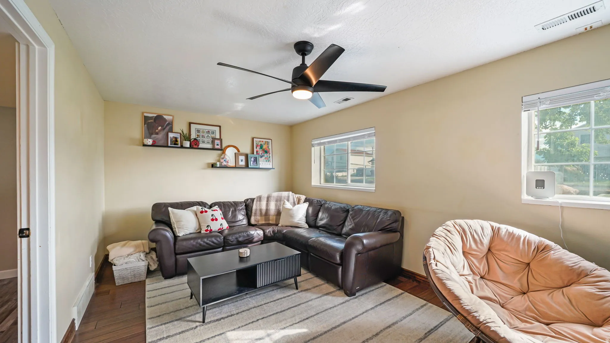 Wood-finish flooring, a ceiling fan with integrated lighting, built-in shelving, and multiple windows