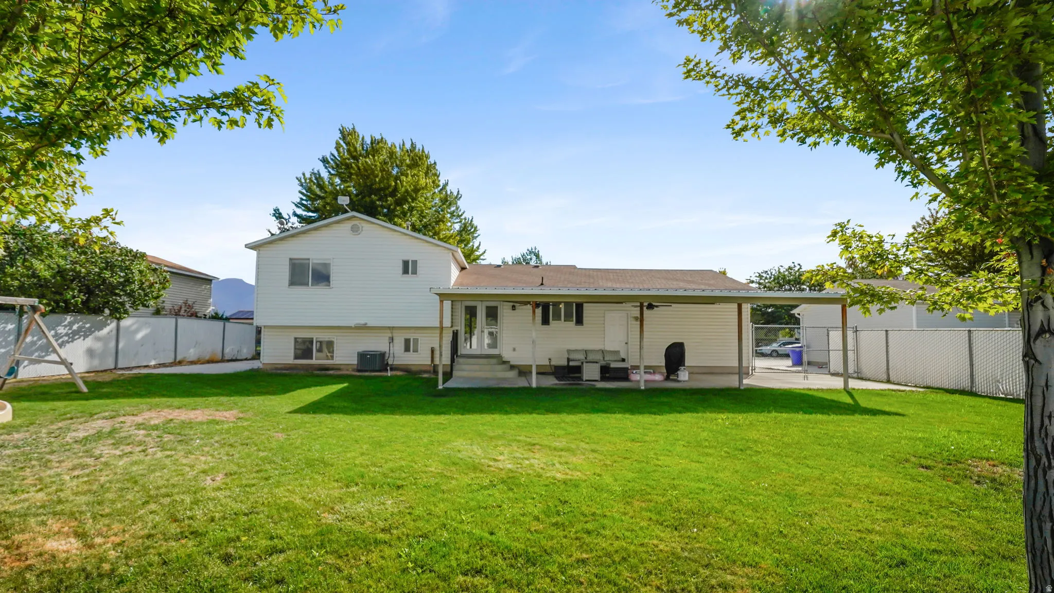 Expansive backyard featuring a large green lawn, covered patio, and mature trees